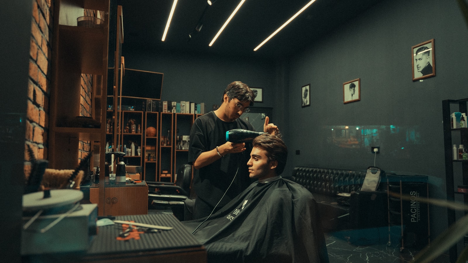 A barber blow-drying and styling a client’s hair inside a barbershop