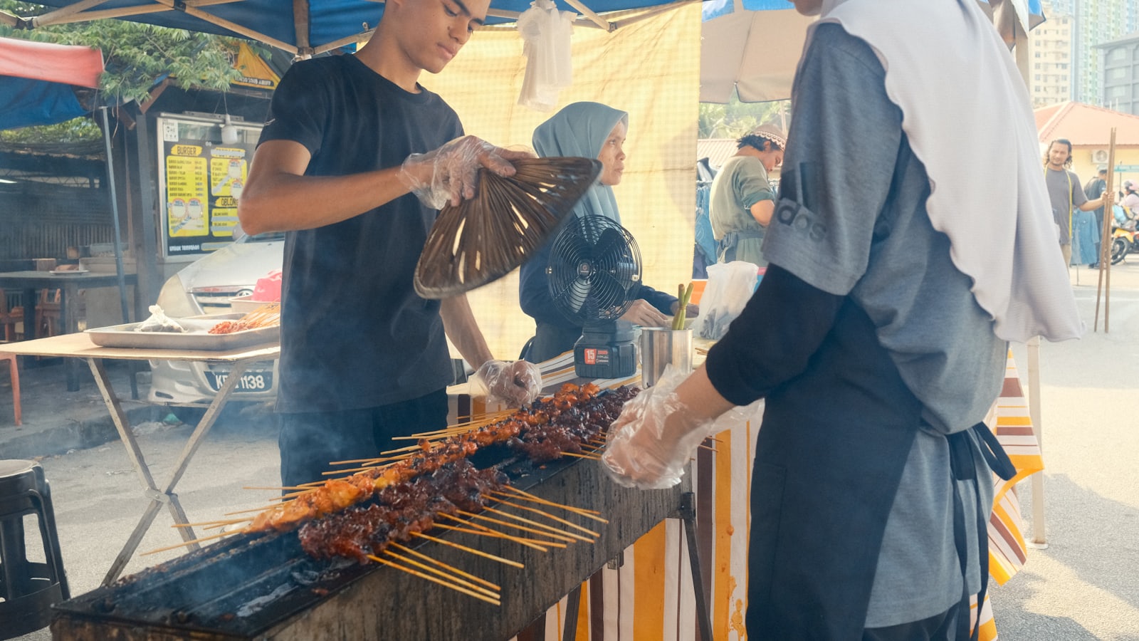 Penjual membakar sate di atas arang pada gerobak makanan pinggir jalan yang ramai
